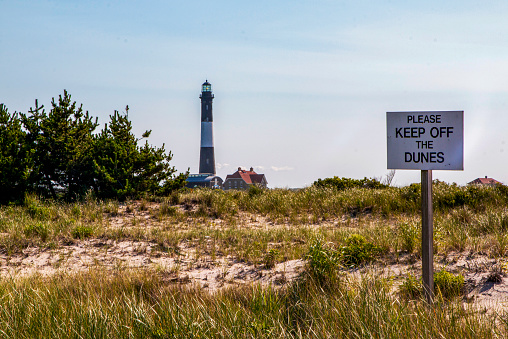 Fire Island Lighthouse in the ditance with a please keep off the dunes sign in the foreground