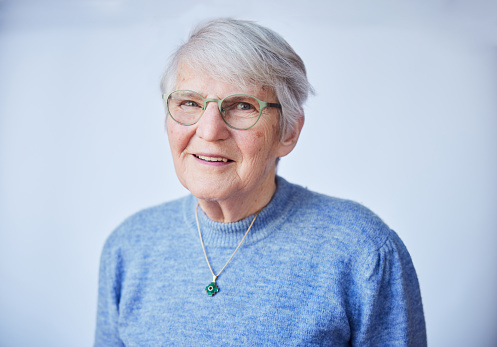 Portrait of a smiling senior woman wearing glasses while standing alone in front of a light background