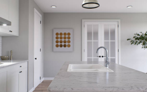 istock Large white kitchen with island and all necessary appliances. 3d rendering. Emphasis on stone countertop with white marble, kitchen sink and doors in the background. 1487779104
