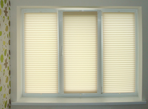 Pleated blinds close-up on the window in the interior. Home blinds - cordless pleated modern shades on apartment windows. Bottom up top down pleated curtains. Beige color fabric. Closed.