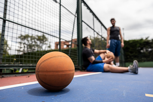 Close-up of a basketball ball over floor in the sports court with young men talking in the background