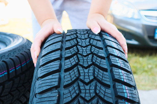 Woman putting hand on new wheel tire. Female holding a tire and standing next to a piles of tires. Auto car repair service