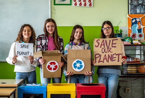 portrait of four teenage girls at school holding signs to save the planet and recycle