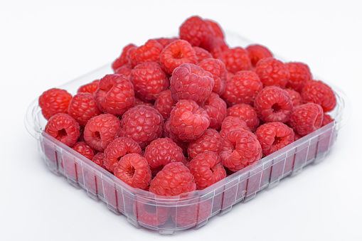 Red ripe raspberries isolated on white background.  A pile of beautiful fruits arranged in a plastic transparent container.