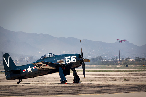 Tucson, Arizona, USA - March 25, 2023: An F-8F Bearcat sits on the tarmac while a biplane performs at the 2023 Thunder and Lightning Over Arizona airshow.