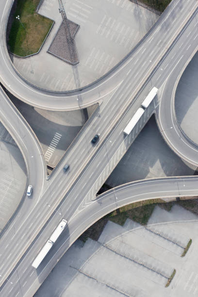 Aerial view of trucks with trailers on a city highway above a large parking lot.