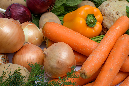 Carrots, onions, potatoes, peppers, greens spread out next to each other.  Fresh, clean and colorful raw vegetables