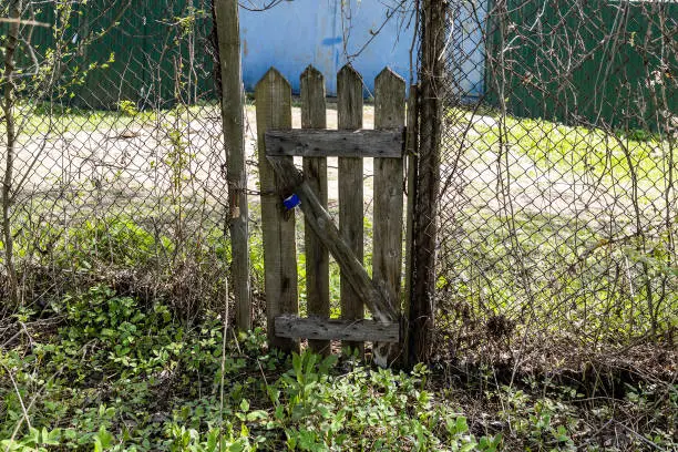 old shabby wooden wicket in chain-link fence in village