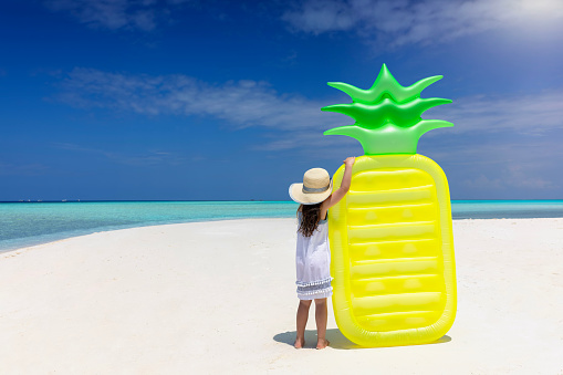 Summer concept with a little girl holding a pineapple shaped floaty on a tropical paradise beach