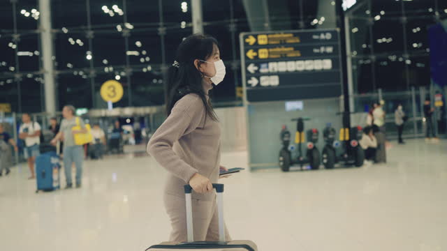 Asian woman passenger wear surgical mask and walking with suitcase luggage at airport terminal