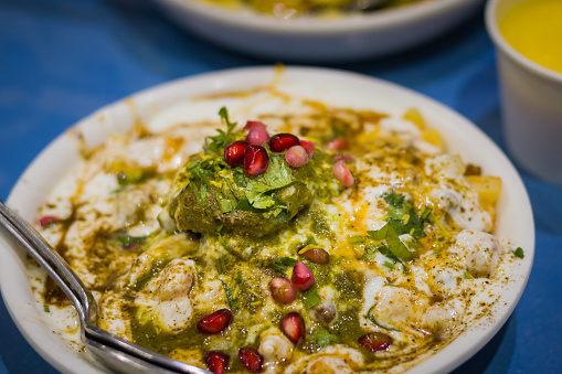 Dahi papri chaat with dahi bhalla served on a plate garnished with Sev, pomegranate seeds and other condiments. Very popular and savoury north Indian dish.