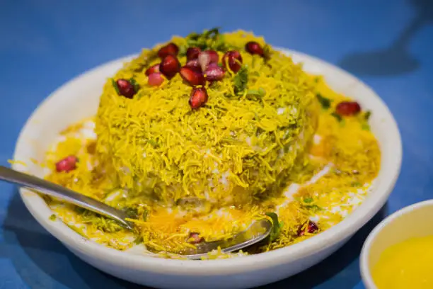 Photo of Dahi vada chaat served on a plate garnished with Sev and pomegranate seeds and other condiments at a restaurant. It is a popular North Indian snack.