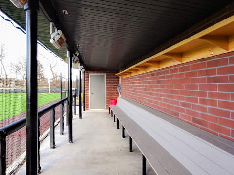 Brick baseball dugout with concrete floor, benches and protective netting.