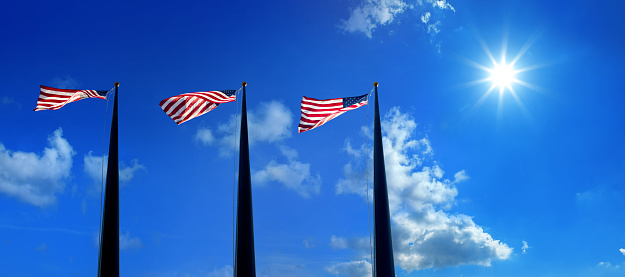 Waving American flags at flagpoles in a row over sunny blue sky and shinning sun