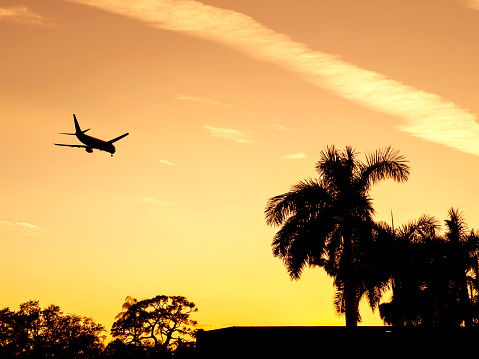 Transportation image of flying commercial passenger airplane over orange colored sunset sky in Florida