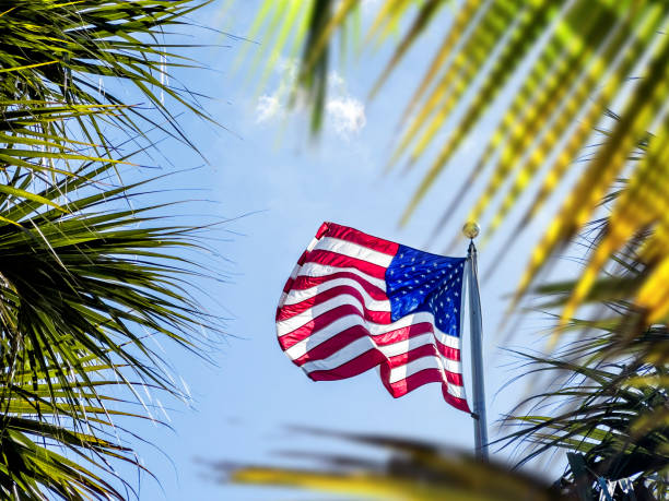 Waving American flag at flagpole over sunny blue sky