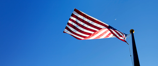 Waving American flag at flagpole over sunny blue sky