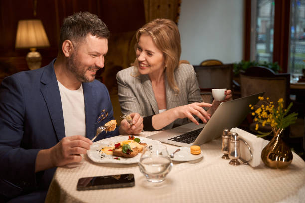 istock Spouses smiling looking at photos from vacation on laptop at restaurant 1487815710