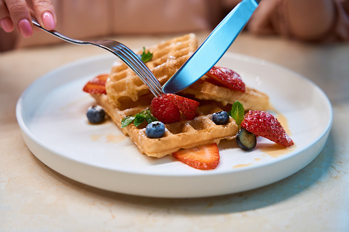 Close-up female hands cutting off piece of waffle with berries ty try, seasonal dish in restaurant