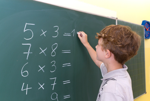 Photo shows a children in front of a blackboard. He solves maths problems. Photo was made in a classroom with studiolight.
