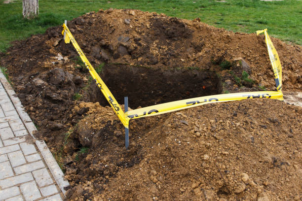 A square pit dug into the soil, next to public sidewalk and fenced with a ribbon, as a sign of danger. Communal service works, eliminate problems underground stock photo