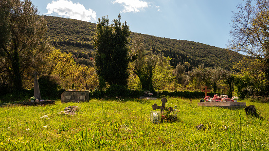 Old graveyard stone crosses and flowers on green lawn grass with hills at background