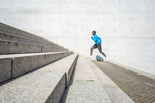 young sportsman running up steps in front of concrete wall outdoors in berlin at sunny day