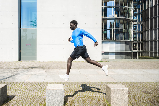 young sportsman jumping on stone blocks in front of concrete wall outdoors in berlin at sunny day