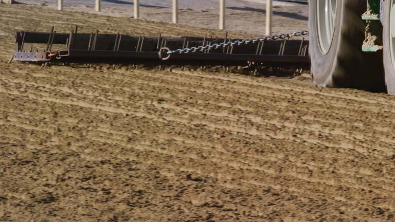 A Tractor Pulls a Groomer along a Dirt Horse Racetrack on a Sunny Day