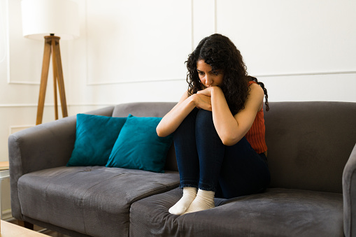 Depressed young woman feeling lonely hugging her knees suffering from depression and mental health problems alone at home