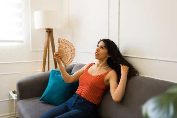 istock Upset hispanic woman feeling hot at home using a fan 1487827544