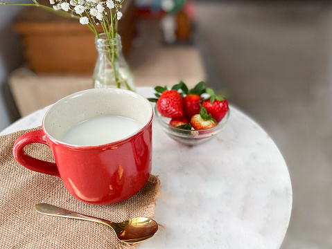 Still life with side table, red coffee cup, strawberries and flowers