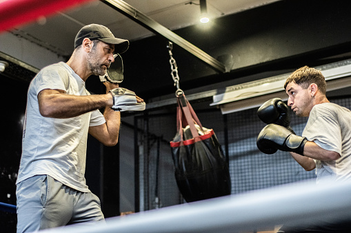 Young man training boxing with his trainer in the ring