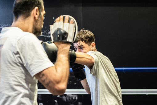 Young man training boxing with his trainer in the ring