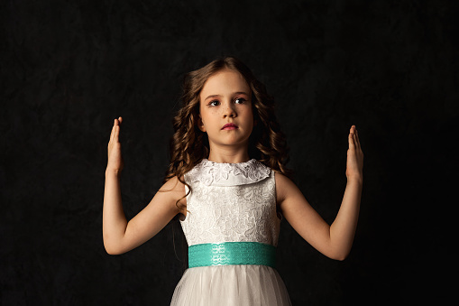 pretty preschool age girl wearing a gold sequined dress and a white bow spinning and twirling in a pale neutral room. She is happy and having fun playing.