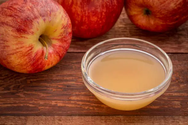 unfiltered, raw apple cider vinegar with mother - a small glass bowl with fresh red apples