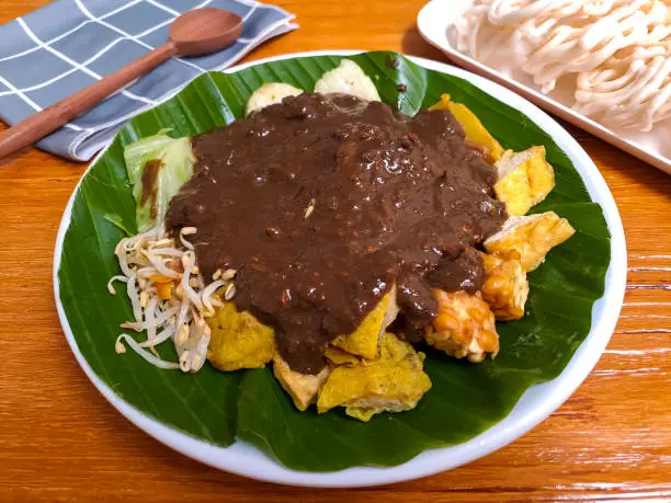 Rujak Cingur, one of indonesian salad from east java which mixed of various type of vegetables, tempeh and cow's nose with peanut sauce. Served in a plate against wooden table, selective focus