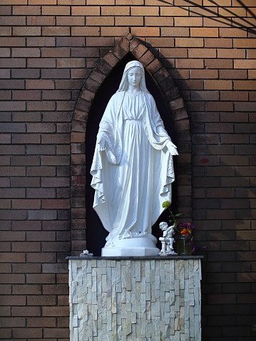 A majestic statue of the Virgin Mary is situated in a peaceful outdoor setting