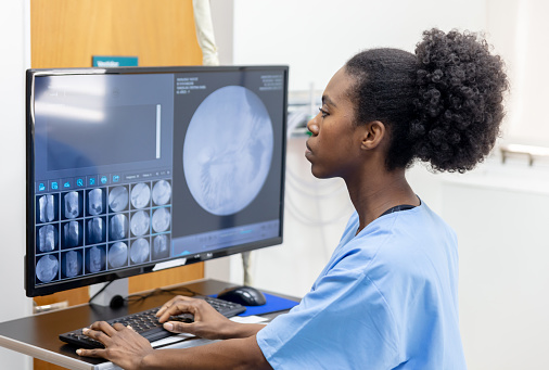 Focused African American female radiologist looking at a patientâs scans to write the report at the clinic - Diagnostics tools concepts