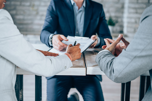 Couple sitting at desk in the bank and signing loan agreement. Shot of three business persons filling in paperwork in an office. Business persons signing a document in board room.