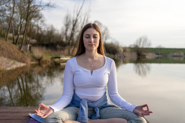 istock Woman relaxingly practicing meditation in nature by the lake. 1487840433