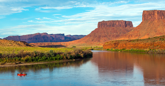 People rafting on Colorado river with table mountains at sunset near Moab, Arches national park, Utah, USA.