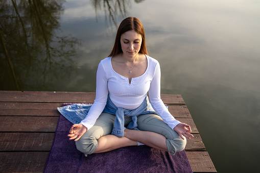 Woman relaxingly practicing meditation in nature by the lake. Nature background. Spiritual and emotional concept. Awakening.