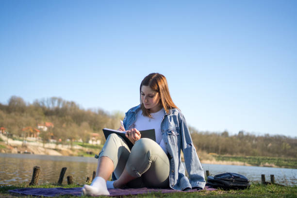 istock Woman at lakeside writing in a notebook. Nature concept. Self reflection. 1487841600