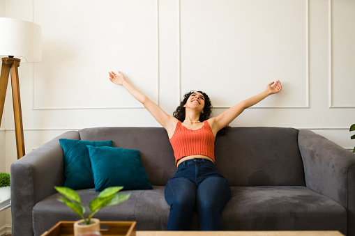 Attractive relaxed young woman feeling carefree and excited while relaxing sitting on the couch in the living room