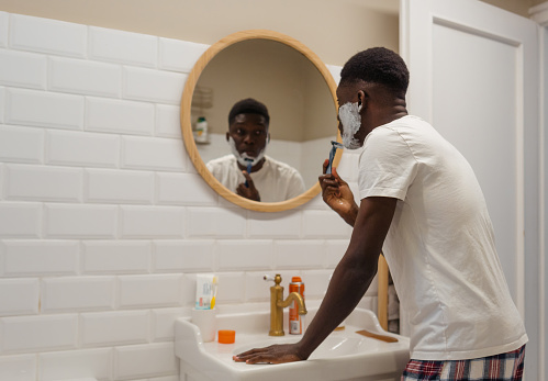 Photo of a young man shaving beard in his bathroom