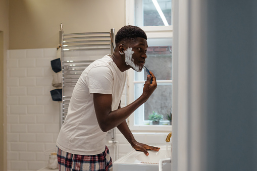 Photo of a young man shaving beard in his bathroom