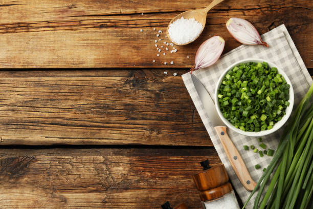 Chopped green onion in bowl on wooden table, flat lay. Space for text