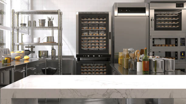 Empty clean white marble top island table in commercial, professional bakery kitchen with stainless steel convection, deck oven, freezer, refrigerator, trolley, cart, bread, bun