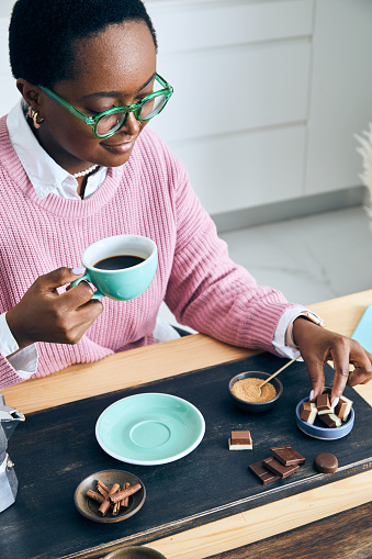 Portrait of a cute and happy young black girl in the kitchen, early bird morning routine, drinking coffee, with chocolate, representing positive mental attitude, wellbeing and a healthy lifestyle, an image with a large copy space